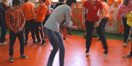 Powiększ grafikę: uczniowie ubrani w barwy pomarańczowe tańczą na sali gimnastycznej