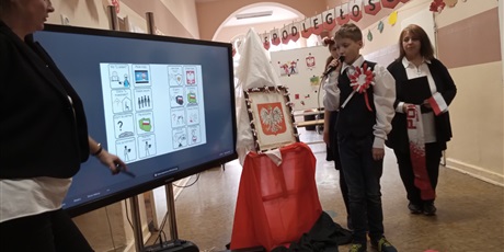Powiększ grafikę: Uczniowie i nauczycielka przy tablicy interaktywnej, w tle dekoracje biało-czerwone