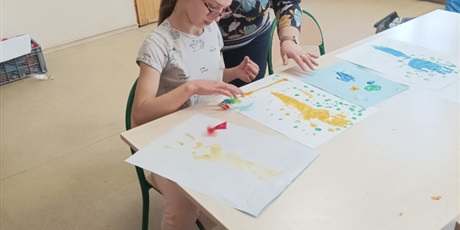 Powiększ grafikę: Uczennica przykleja kolorowe piórka z pomocą nauczyciela