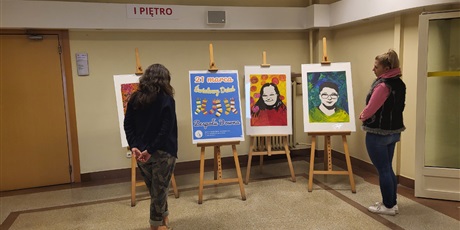 Powiększ grafikę: Portrety wychowanków ośrodka oraz plakat dnia osób z Zespołem Downa na stelarzach, oglądane przez zwiedzających