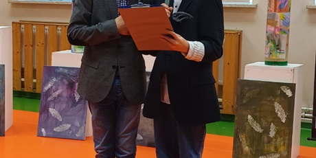 Powiększ grafikę: Dwóch uczniów recytuje wiersz na akademii, w tle dekoracje.