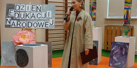 Powiększ grafikę: Nauczycielka trzyma mikrofon i zapowiada kolejnych artystów, w tle dekoracje.