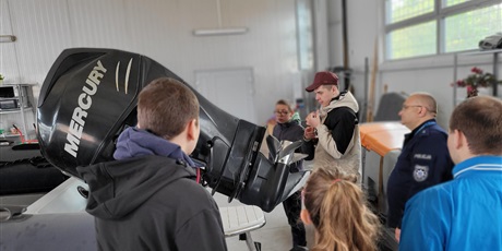 Powiększ grafikę: Grupa chłopców i dziewczynka oglądają silnik motorówki policyjnej.