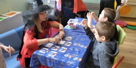 Powiększ grafikę: Nauczycielka wraz z dziećmi siedzą przy stoliku I układają wróżby.