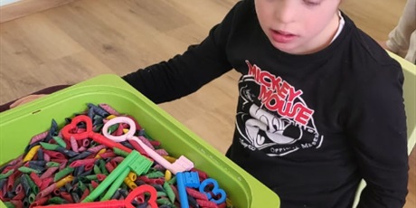 Powiększ grafikę: Chłopiec siedzi przy stoliku przed nim znajduje się pojemnik z makaronem a nim ukryte klucze