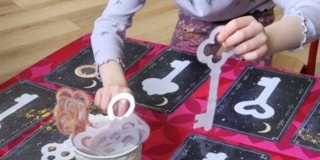 Powiększ grafikę: Chłopiec siedzi przy stoliku I dopasowuje klucze do wzoru na karcie.