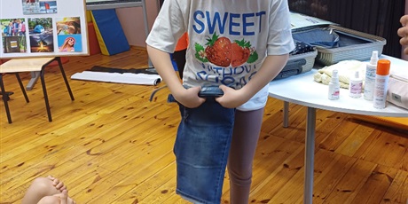 Powiększ grafikę: Dziewczynka składa krótkie spodenki. W tle na stole otwarta walizka i kosmetyki wakacyjne.