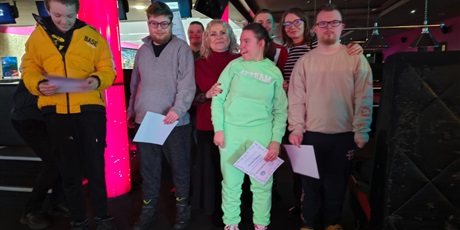 Powiększ grafikę: Zdjęcie zbiorowe z wręczenia dyplomów i nagród za udział w spotkaniu, w tle sala bowlingowa.