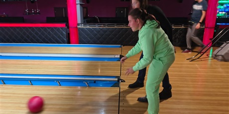 Powiększ grafikę: Widok z boku: dziecko oburącz rzuca kulą po torze, w tle inny zawodnik.