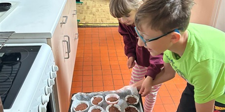 Powiększ grafikę: Chłopiec z dziewczynką wkładają przygotowane muffiny do piekarnika.