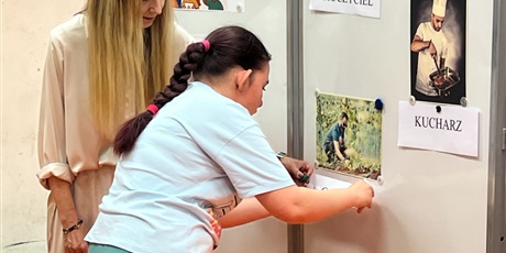Powiększ grafikę: Dziewczyna z kobietą przypinająetykietę z napisem pod ilustracją ogrodnika na tablicy magnetycznej.