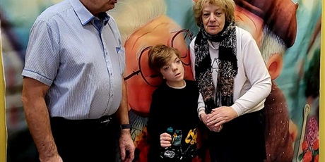 Powiększ grafikę: 1.	Chłopiec stoi z dziadkami na tle banera przedstawiający Babcię i Dziadka.