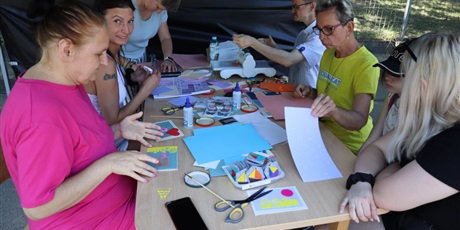 Powiększ grafikę: Grupa ludzi wycina z kolorowego papieru przy stole w namiocie.