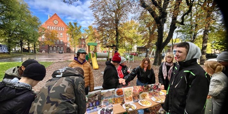 Powiększ grafikę: Dzieci siedzą przy stole wraz z wychowawcami. Na stole stoją miski z różnym produktami. Jest miska z budyniem, kisielem, krochmalem, ziemniakami i obierkami ziemniaczanymi. Dzieci dotykają produktów d
