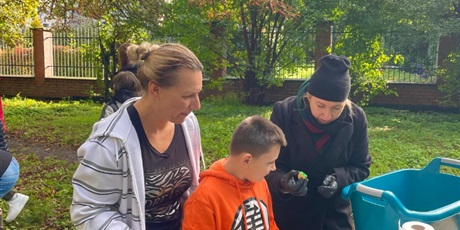 Powiększ grafikę: Chłopiec stoi z dorosłymi przy stole. Chłopcu jest przybijana zielona pieczątka bo udało mu się znaleźć ukrytego ziemniaka.