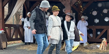 Powiększ grafikę: Na pierwszym planie trzech chłopców w strojach pastuszków tańczy, w tle stajenka. 