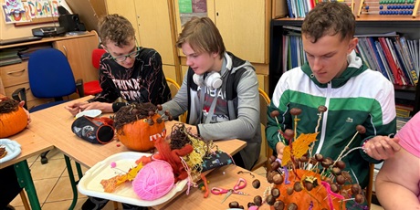 Powiększ grafikę: Trzech chłopców siedzi przy stole.  Na stole stoją przystrojone przez nich dynie Wspólnie dekorują je