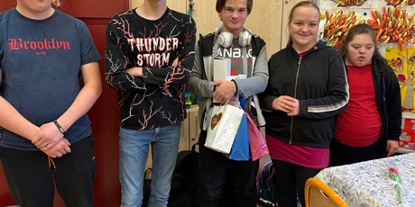 Powiększ grafikę: Troje chłopców i dwie dziewczynki stoją i uśmiechają się, jeden z chłopców trzyma torebki z prezentami.