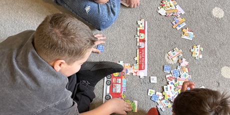 Powiększ grafikę: trzech chłopców na dywanie składa wspólnie wieloelementowe puzzle dotyczące straży pożarnej.
