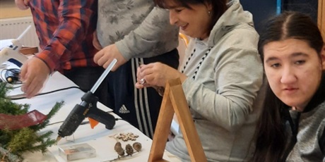 Powiększ grafikę: opiekunowie wraz ze swoimi podopiecznymi wykonują ozdobę – świąteczny stroik z bombek, drewna i gałęzi świerkowych