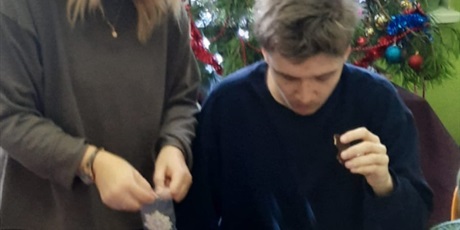 Powiększ grafikę: uczeń z mamą tworzą świąteczny wianek wykorzystując styropianowe obręcze, włóczkę i bombki