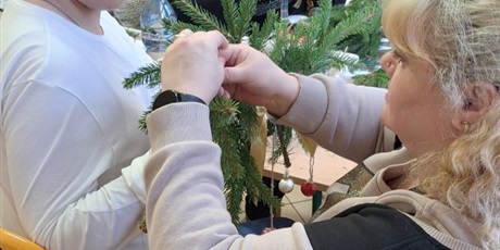 Powiększ grafikę: uczeń z mamą i siostrą tworzą stroik świąteczny ze świerkowych gałązek