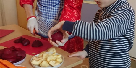 Powiększ grafikę: Pani kroi buraki na kawałki i podaje chłopcu, na talerzyku są p[rzygotowane kawałki jabłek. Będzie sok buraczkowo- jabłkowy.