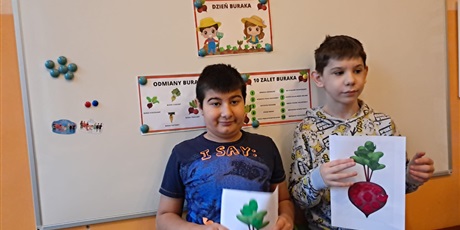 Powiększ grafikę: Dwóch chłopców stoi na tle tablicy i pokazuje wykonane prace z buraka, wylepianka z plasteliny.