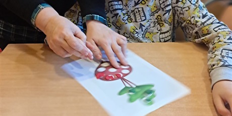 Powiększ grafikę: Pani pokazuje chłopcu jak wylepiać białe kropki w obrazku buraka plasteliną kolorystycznie dobraną do buraka.