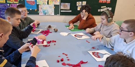 Powiększ grafikę: Zdjęcie zbiorowe. Grupa uczniów przy wspólnym stole wykonuja prace plastyczne. Kontur buraka wylepiają bibułą lub rwą bibułę.