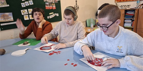 Powiększ grafikę: Zbliżenie na trzech chłopców, którzy wylepiają kontur buraka porwanym na kawałki papierem kolorowym.