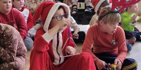 Powiększ grafikę: Chłopiec w stroju Mikołaja gra na trójkącie. W tle widać uśmiechnięte dzieci.