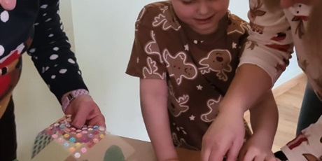 Powiększ grafikę: Chłopiec w koszulce w pierniczki wykleja choinkę.