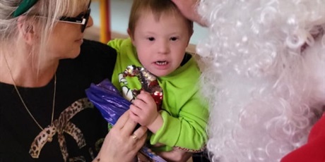 Powiększ grafikę: Przeczkolak siedzi na kolanach u nauczycielki. Mikołaj wręcza mu prezent.