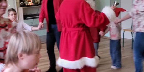 Powiększ grafikę: Przedszkolaki tańczą trzymając się za ręce. Między dziećmi stoi Mikołaj.