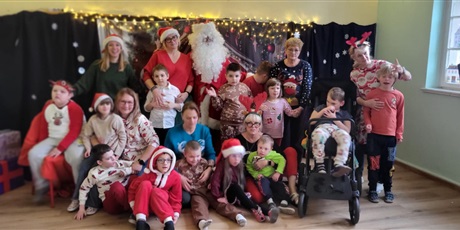 Powiększ grafikę: Przedszkolaki, nauczycielki i Mikołaj pozują do zdjęcia. W tle świąteczne dekoracje i chionka.