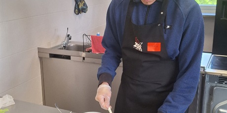 Powiększ grafikę: chłopiec przy blacie kuchennym smaruje kanapki leżące na desce do krojenia masłem