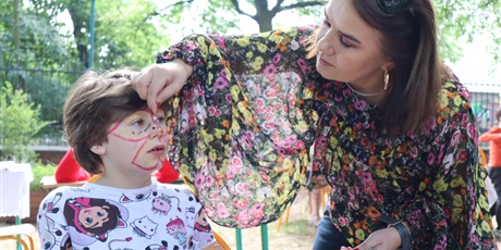 Powiększ grafikę: Kobieta malująca twarz dziecka . Na drugim planie drzewa 