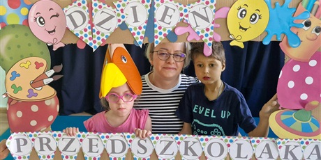 Powiększ grafikę: Nauczycielka z chłopcem i dziewczynką w fotobudce z napisem "dzień przedszkolaka "