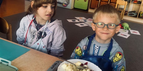 Powiększ grafikę: 5.	Dziewczynka z chłopcem siedzą przy stoliku, przed chłopcem stoi talerz z gotowa sałatką.