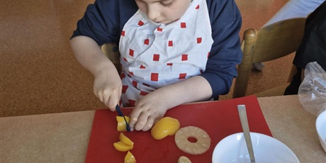 Powiększ grafikę: Chłopiec siedzi przy stole i kroi owoce.