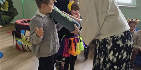 Powiększ grafikę: Wychownek pasowany przez panią dyrektor dużym ołówkiem. W tle wystrój i inne dzieci.