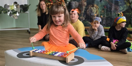 Powiększ grafikę: Wychowanka gra na cymbałkach i uśmiecha się. W tle inne dzieci i dekoracja.