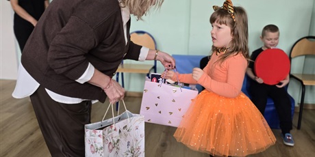 Powiększ grafikę: Wychowanka odbiera prezent od pani dyrektor z okazji pasowania. W tle ściana i dziecko siedzące na krześle.