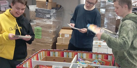 Powiększ grafikę: Uczniowie układają i segregują książki. w tle kartony.
