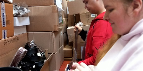 Powiększ grafikę: Uczniowie na terenie magazynu zakładają zabezpieczenia antykradzieżowe na odzież