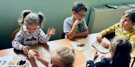 Powiększ grafikę: 9.	Dzieci siedzą przy stolikach, przed nimi leżą zdjęcia jeży i materiały do ich wykonania.