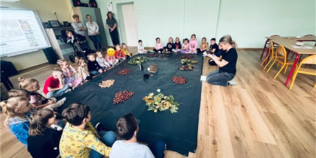 Powiększ grafikę: 5.	 Dzieci siedzą na podłodze, wokół ścieżki sensorycznej złożonej z liści, kasztanów, orzechów i szyszek. Przed nimi siedzi nauczycielka i mówi wiersz o jeża, bohaterze zajęć.