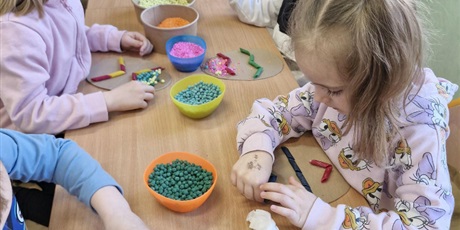 Powiększ grafikę: 4.	Dziewczynka siedzi przy stoliku I wypełnia tekturowe jajko materiałami sypkimi t.j ryż I cieciorka. 