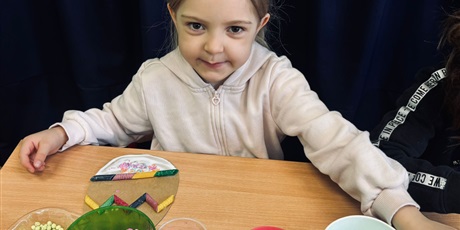 Powiększ grafikę: 7.	Dziewczynka siedzi przy stoliku, przed nią ustawione są materiały w maseczkach, z których będzie przygotowywała swoją pracę.